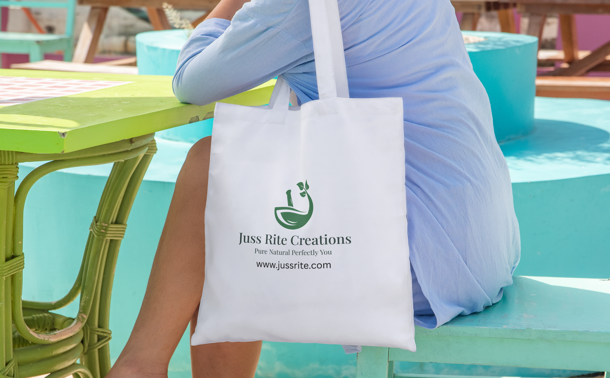 Person sitting at a table with a white tote bag featuring 'Juss Rite Creations' branding.